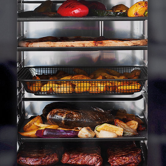 Interior view of a HOBART CHEF'S COMBI oven with multiple racks – loaded with grilled vegetables, pizza, potato wedges, roast with vegetables, and steaks, all cooked simultaneously and evenly.