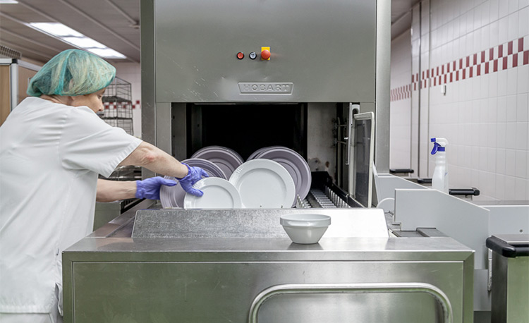 Loading dishes into a HOBART dishwasher in a modern dishwashing area, part of a FLOW Line autoLINE, automatic washing system for efficient cleaning of plates and bowls, stainless steel design for hygienic and optimized workflows.